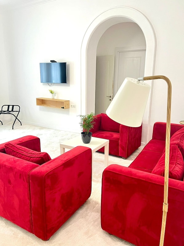 Uma sala de estar moderna com sofás vermelhos, uma mesa de centro branca, um abajur, uma televisão e uma planta.