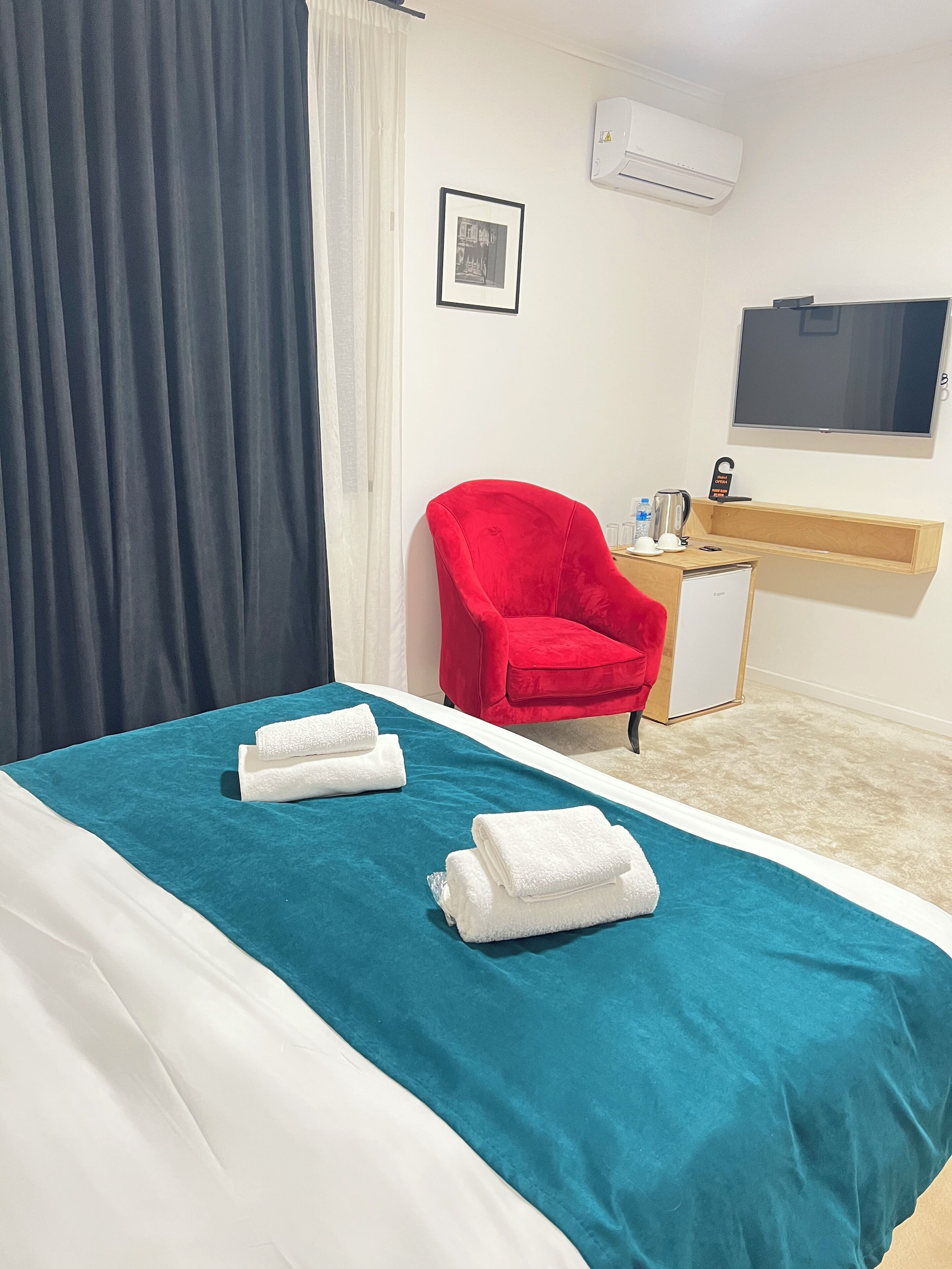 Ein Hotelzimmer mit einem Bett, einem roten Sessel, einem Schreibtisch mit Wasserkocher und einem Flachbildfernseher.
