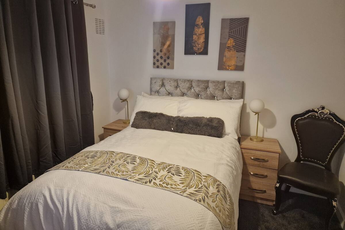 A bedroom with a bed, two bedside tables, a chair, and artwork on the wall.