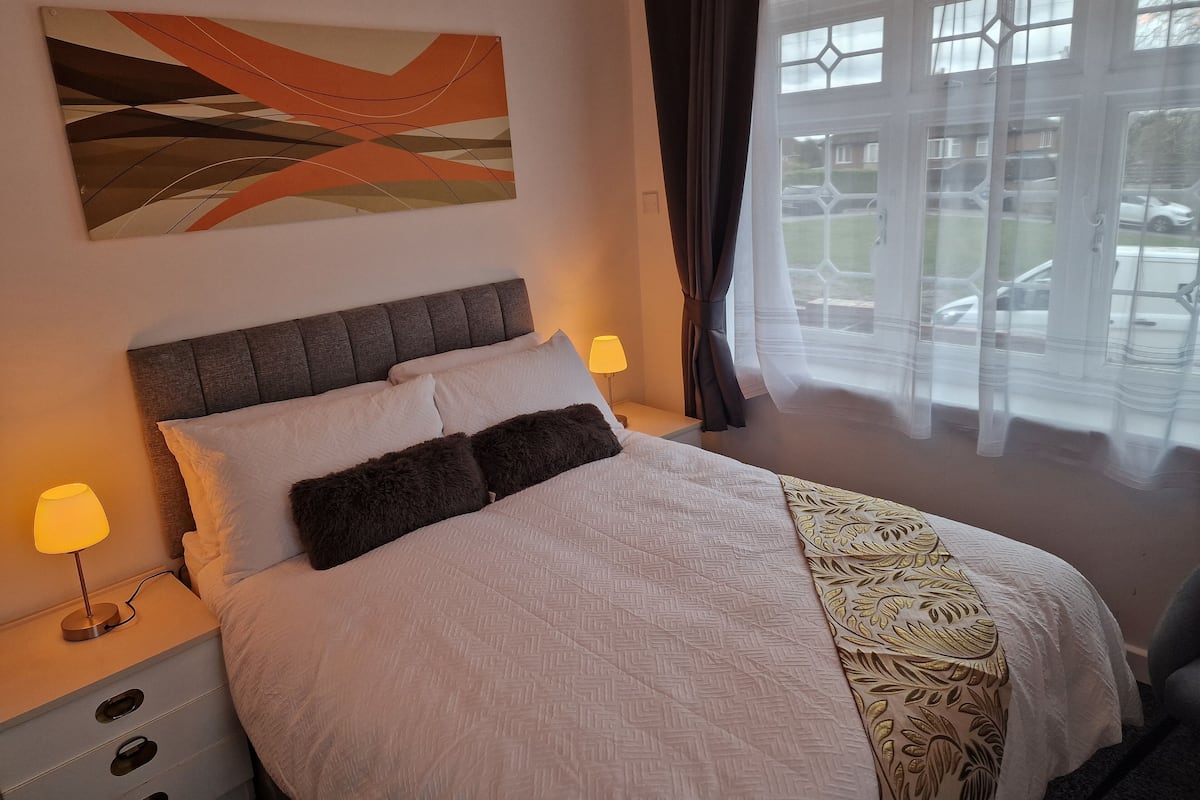 A neatly made bed with a patterned bedspread, a headboard, and two bedside lamps.