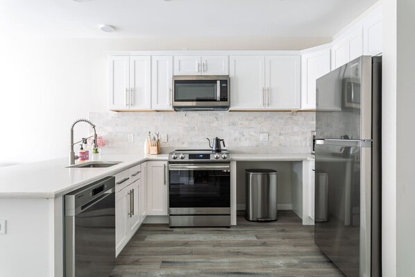 A modern kitchen with white cabinetry, stainless steel appliances, and a herringbone wood floor.