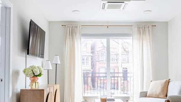 A modern, well-lit room with a large window, a dining area, and a TV mounted on the wall.