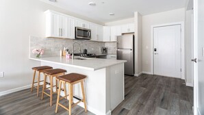 A modern kitchen with white cabinets, a stainless steel refrigerator, and a central island with stools.