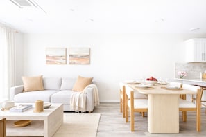 Una sala moderna con sofá, mesa de centro y comedor con sillas y una mesa lista para dos personas.