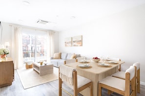 Una sala de estar moderna con comedor, un juego de sofá, una mesa de centro y vistas de la ciudad a través de amplios ventanales.