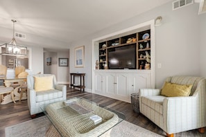 A living room with a sofa, armchairs, a coffee table, a television, and a cabinet with decorative items. - Quiet Oceanfront Condo & Hot Tub, Steps to Coligny (Hilton Head Island)