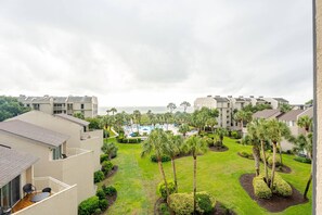 A residential building with a pool, surrounded by palm trees and a view of the ocean.