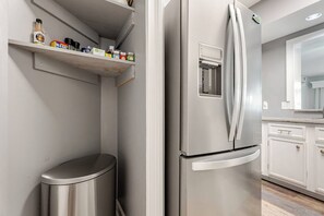Eine moderne Küche mit einem Edelstahl-Kühlschrank, einer Mülltonne und einem Regal mit verschiedenen Gegenständen.