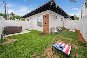 A modern house with a white exterior, a wooden door, a small window, and a patio area with a lawn and a flag.