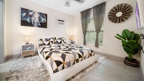Une chambre à coucher avec un lit, un ventilateur de plafond, un climatiseur fixé au mur, une grande fenêtre avec des rideaux et une plante en pot.