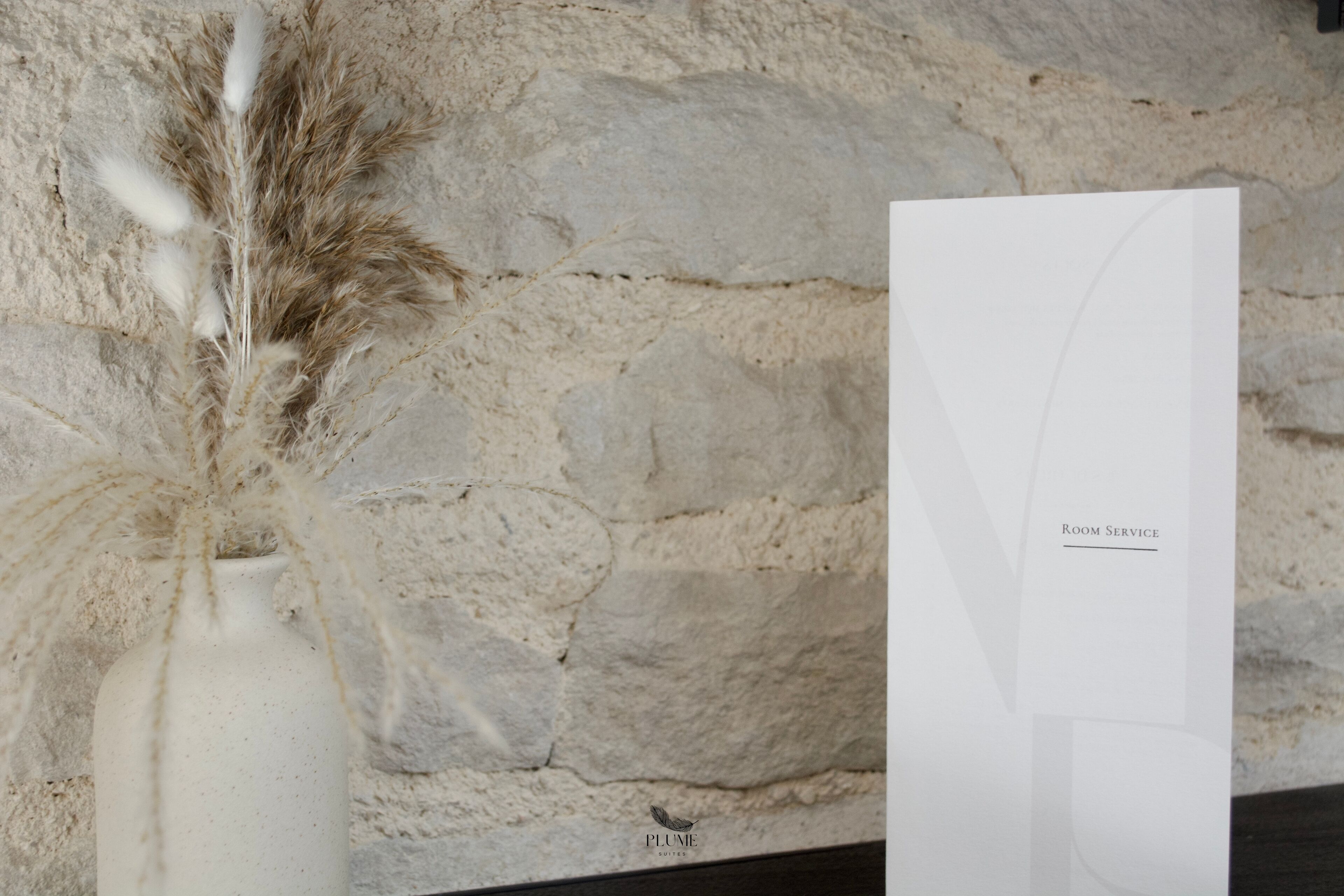 A white vase with pampas grass and a white card with "Room Service" text.