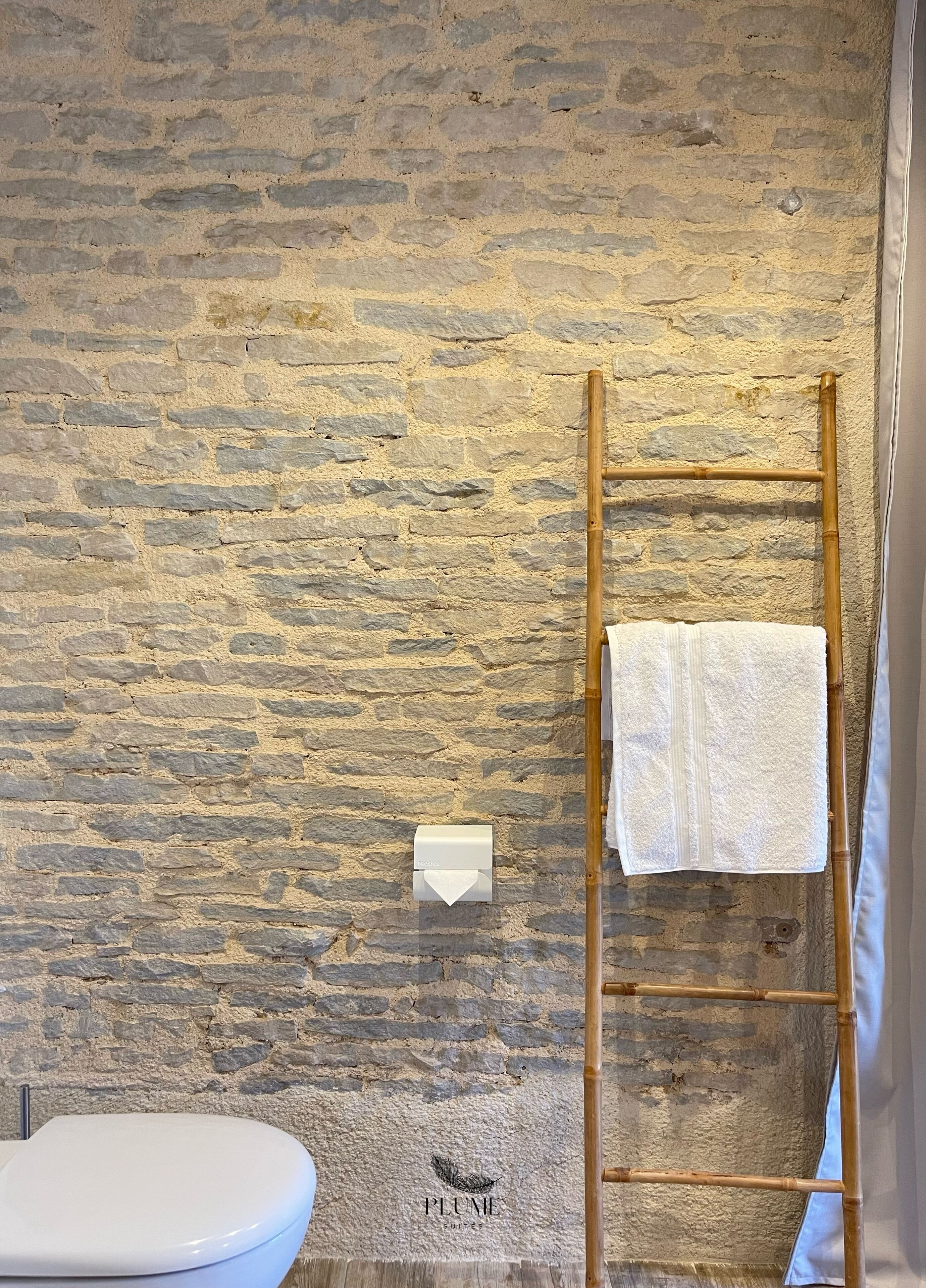 Un baño con pared de piedra, un inodoro y una escalera de madera con una toalla colgada.