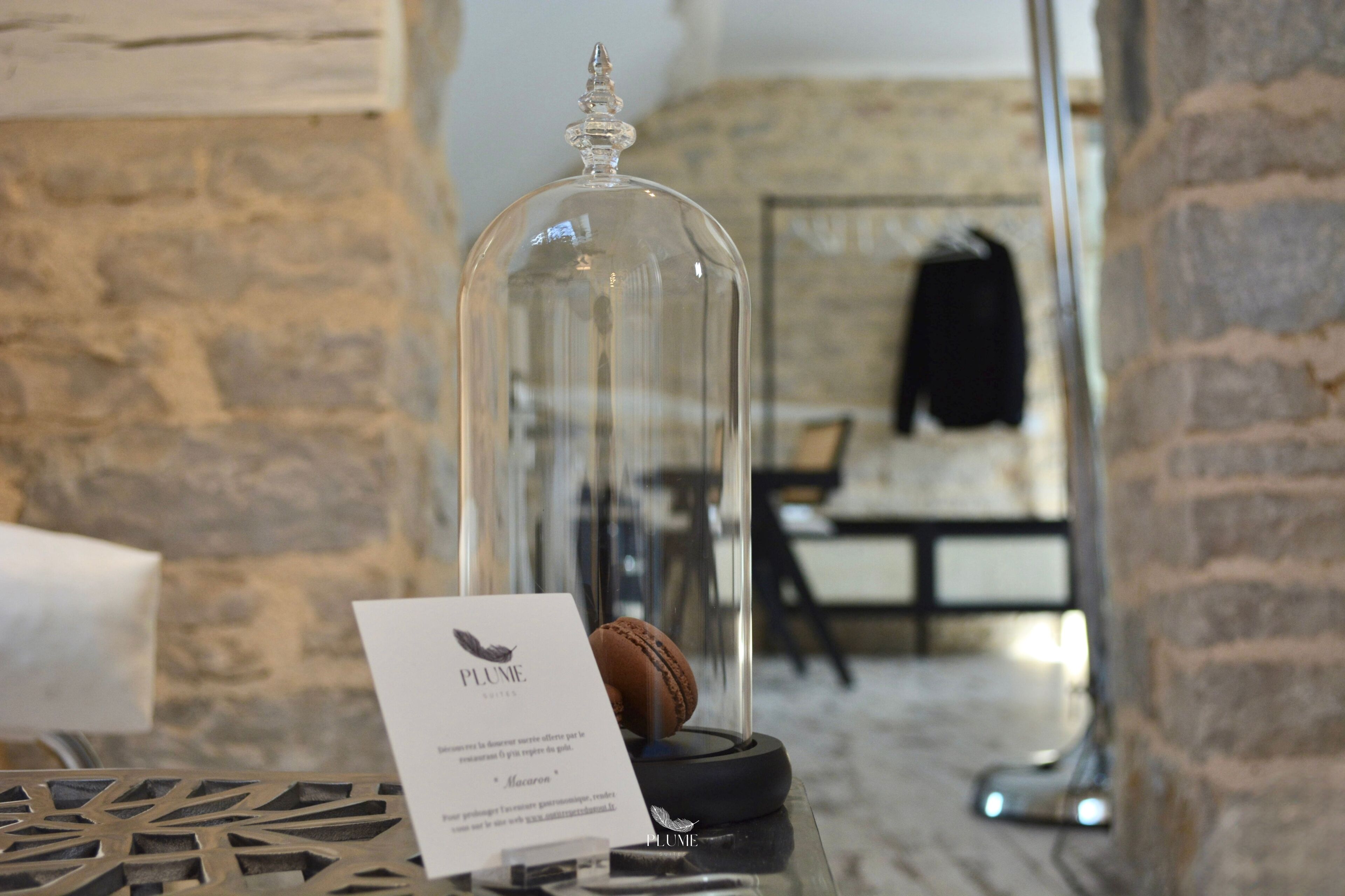 A glass dome display with a macaroon and a sign labeled "PLUME."