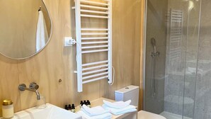 Un baño moderno con tocador de madera, un espejo grande, toallero, cabina de ducha y un inodoro.