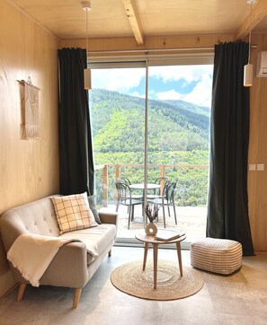 Une pièce confortable avec un canapé, une petite table et une vue sur une montagne boisée.