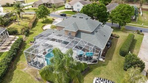 A residential property with a large glass-enclosed swimming pool, a tennis court, and a chessboard in the yard.