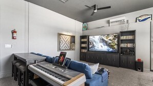 A living room with a piano, blue sofa, TV, bookshelf, and a ceiling fan.