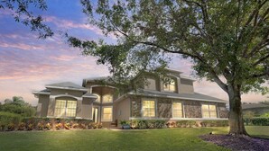 A modern two-story house with a stone facade, large windows, and a well-maintained lawn.