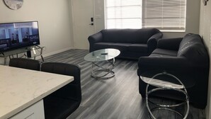 A living room with a dark-colored sofa, a glass coffee table, and a television on a glass stand.
