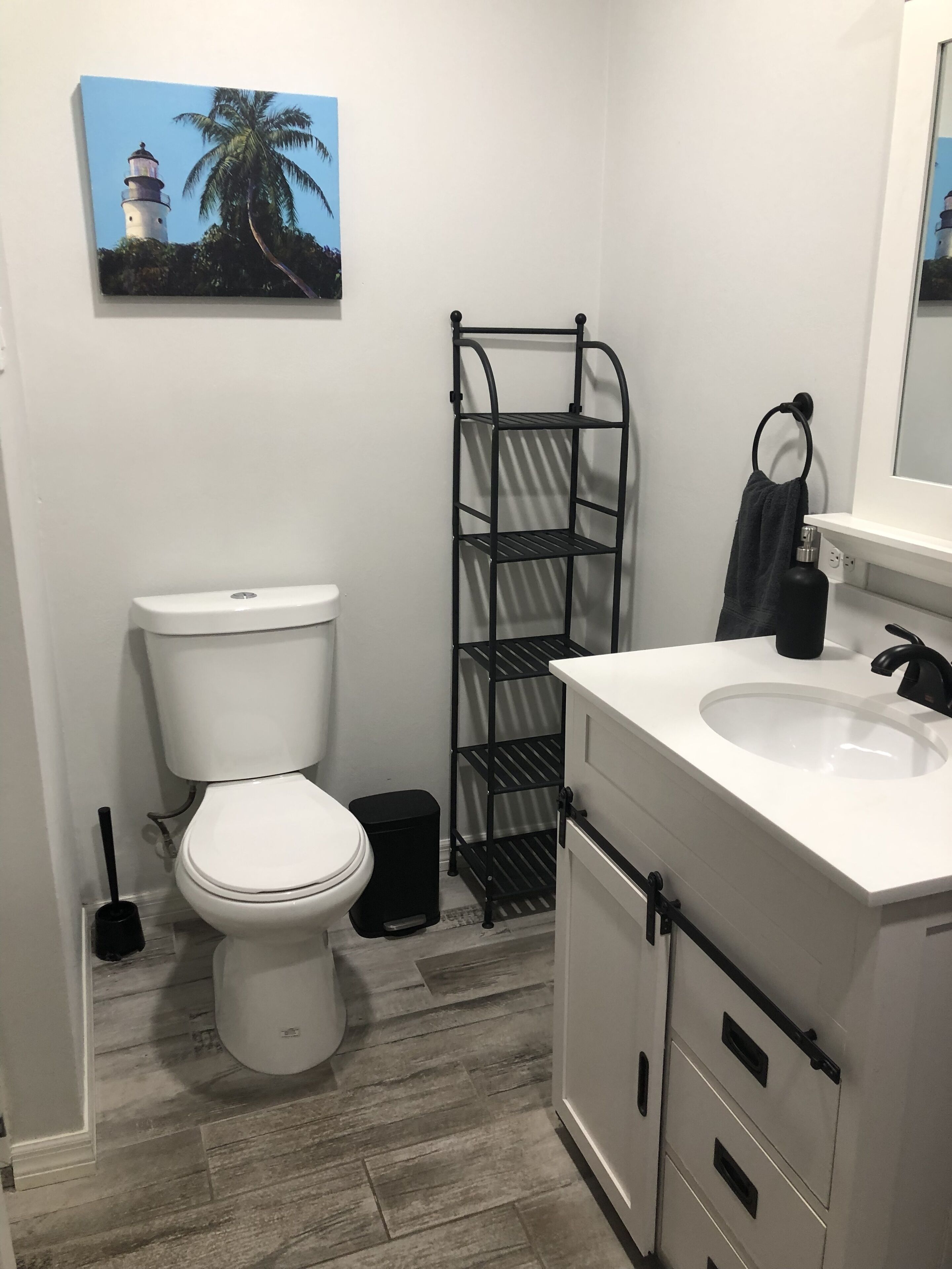 Ein Badezimmer mit Toilette, Waschbecken, Handtuchhalter und einem schwarzen Metallregal.
