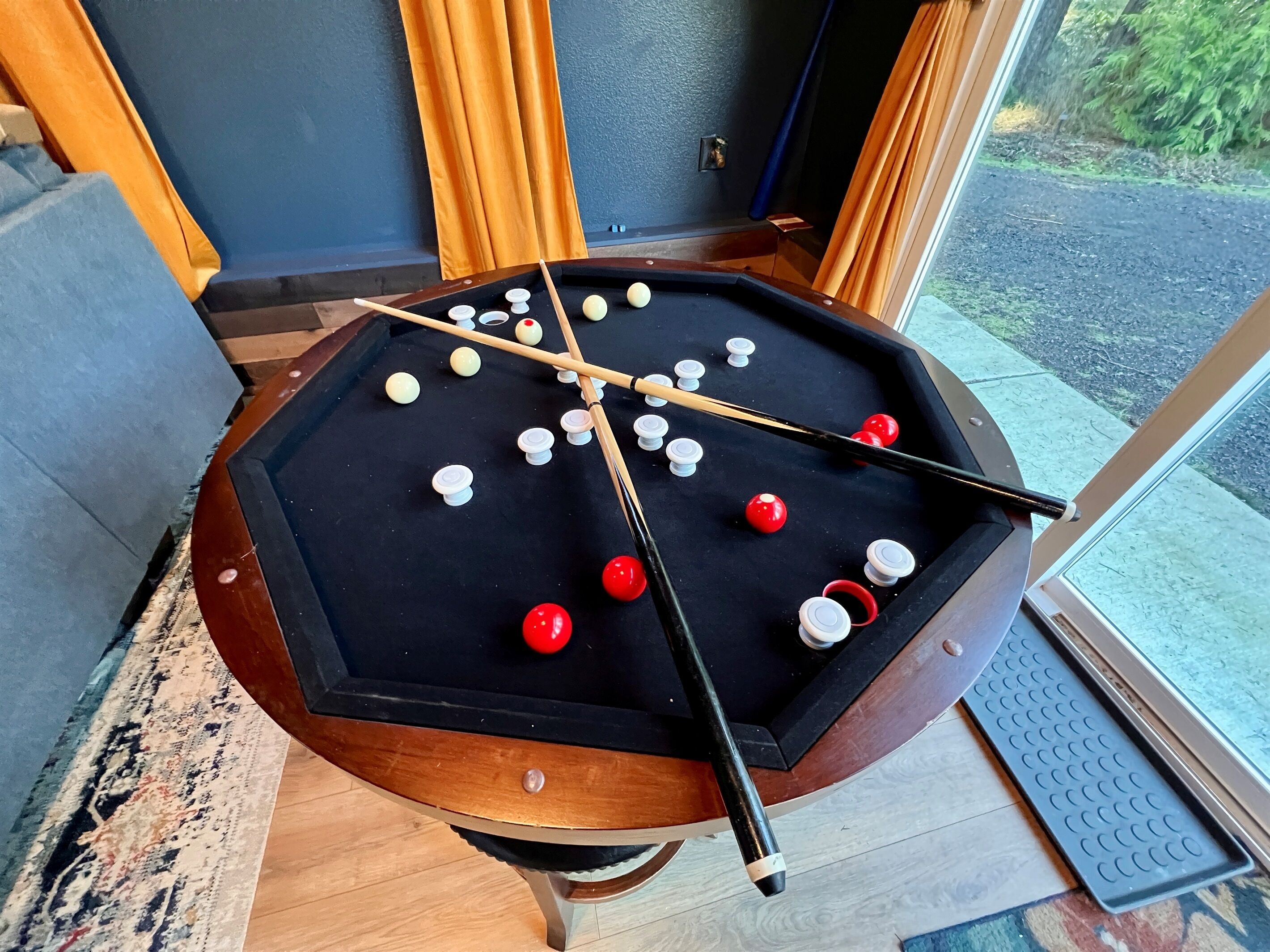 A pool table with balls and cues, surrounded by wooden furniture and a patterned rug.