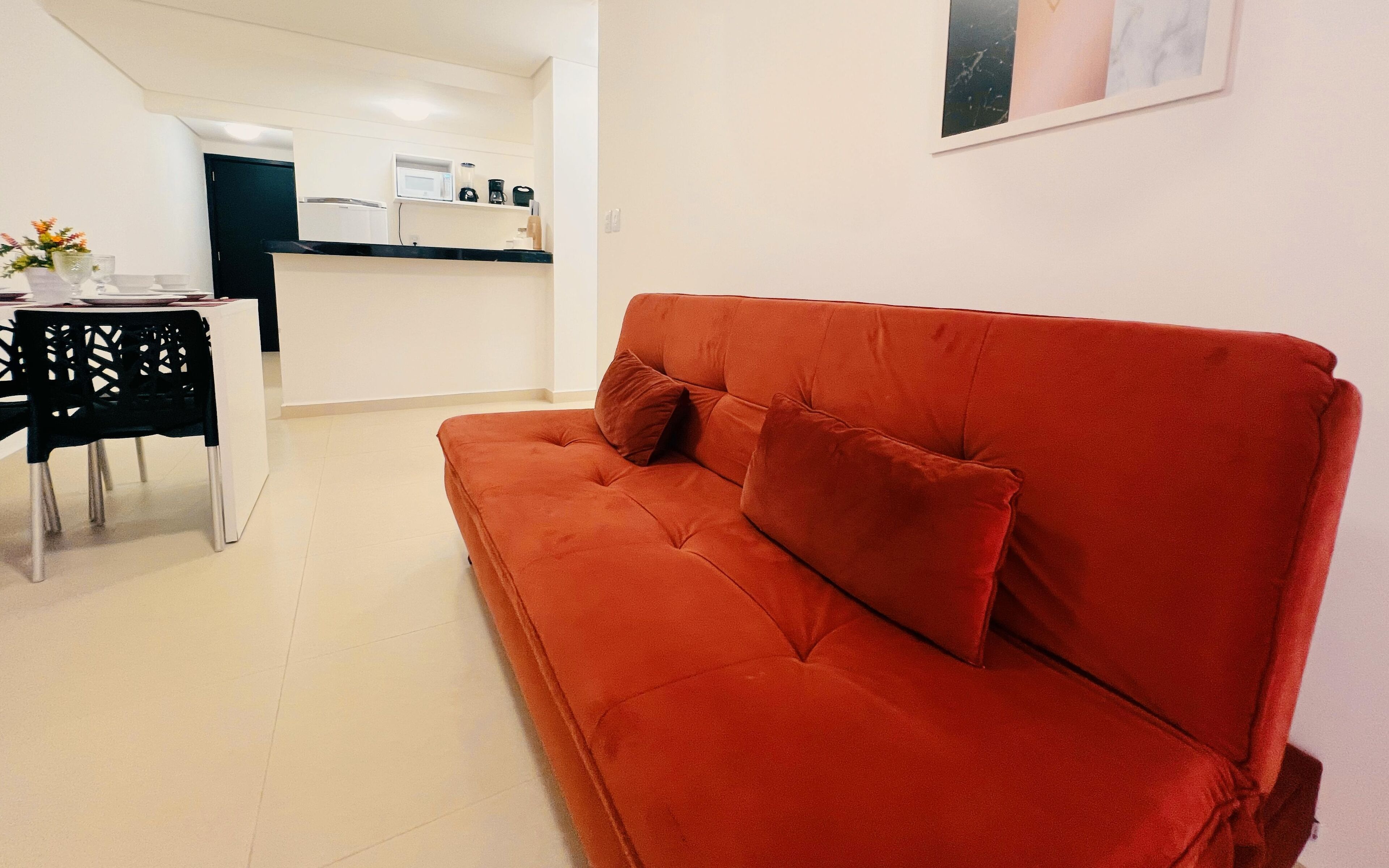 En rød sofa med to puder i et moderne, minimalistisk opholdsrum med et køkken i baggrunden.