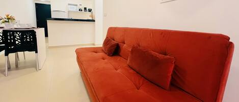 En rød sofa med to puder i et moderne, minimalistisk opholdsrum med et køkken i baggrunden.