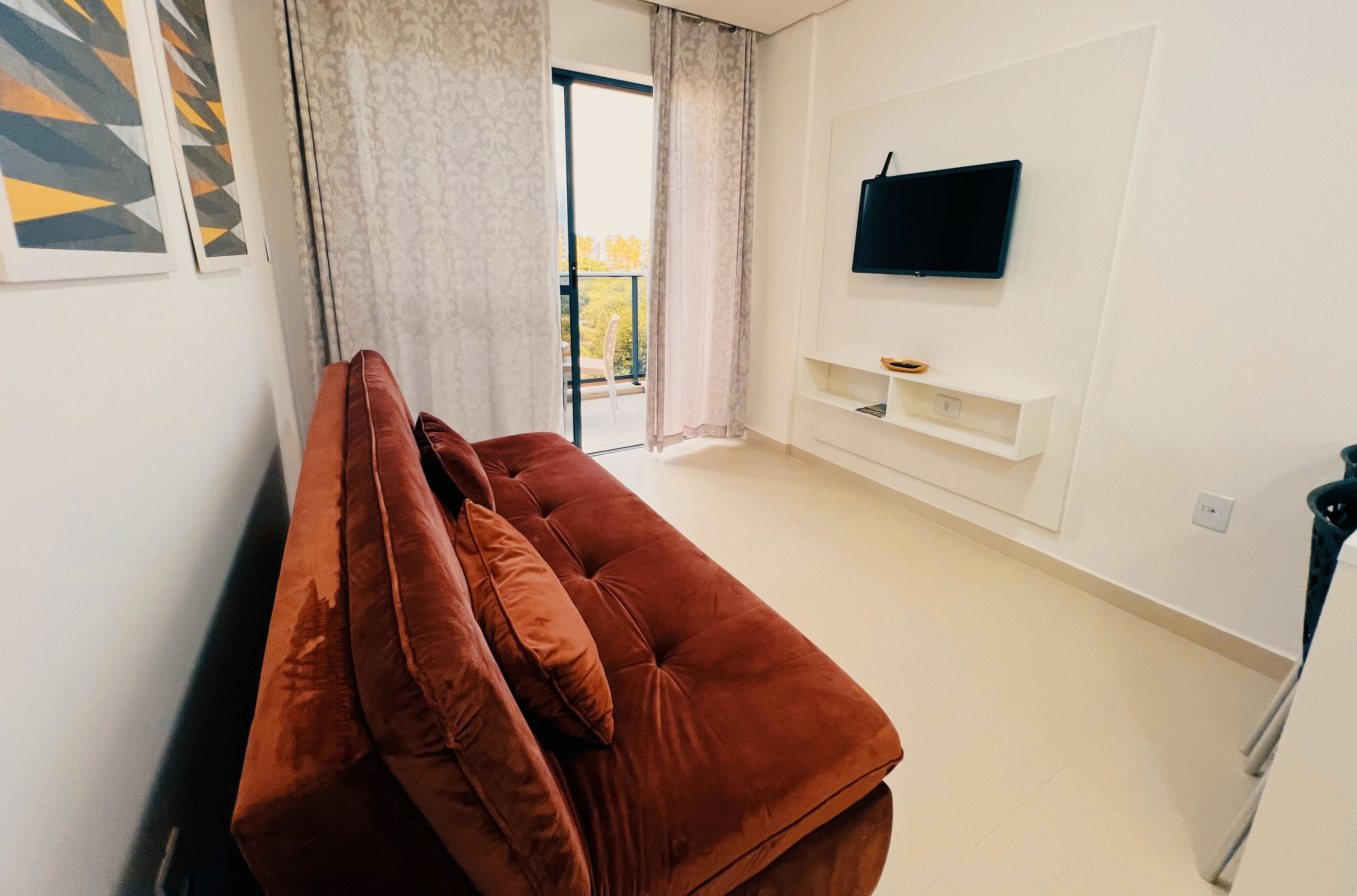 Ein modernes Wohnzimmer mit einem braunen Sofa, einem flachbildfernseher an der Wand und einer Glastür, die auf einen Balkon führt.