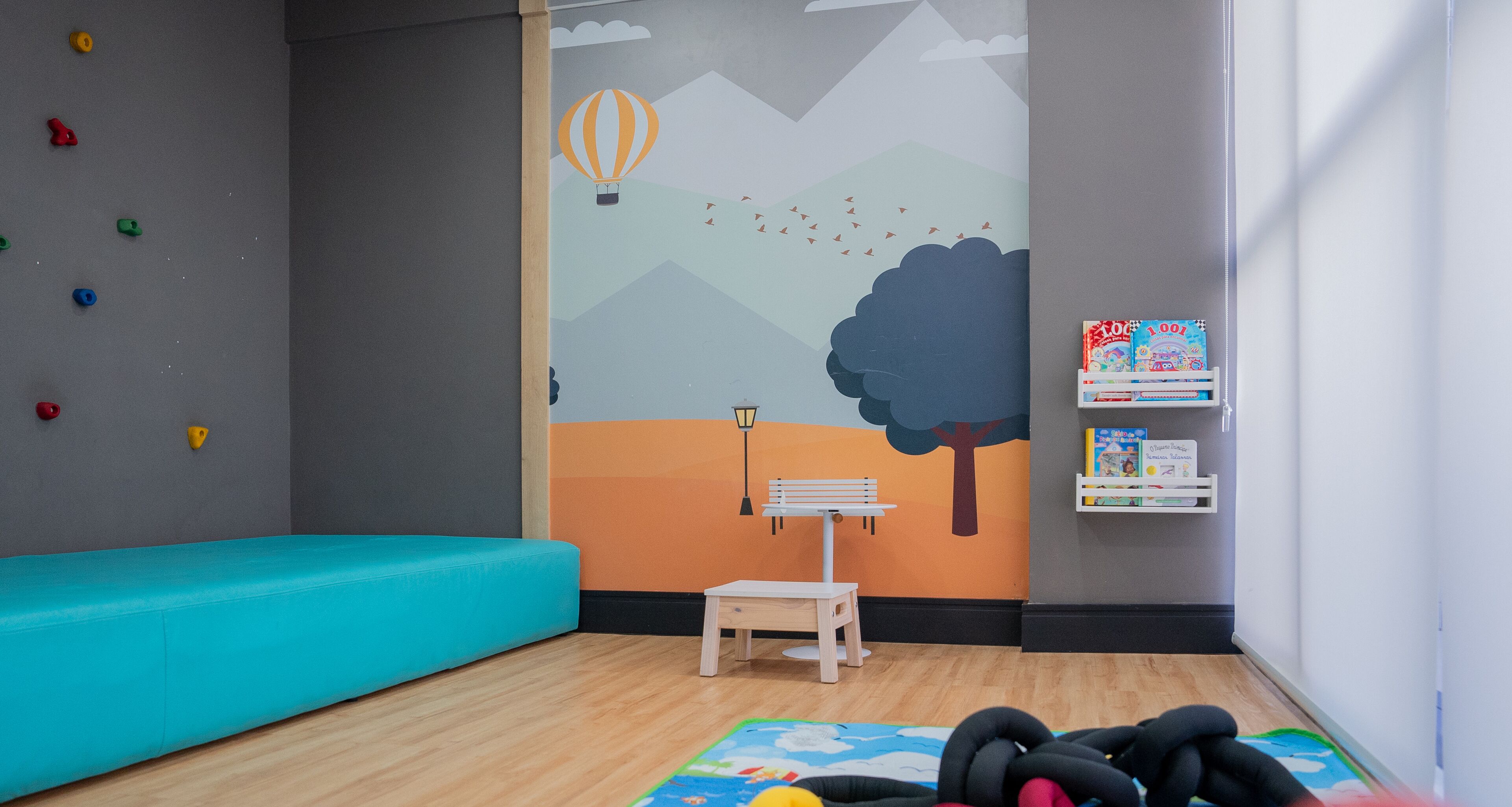 A children's playroom with a climbing wall, a colorful mural, a teal sofa, and a small table.