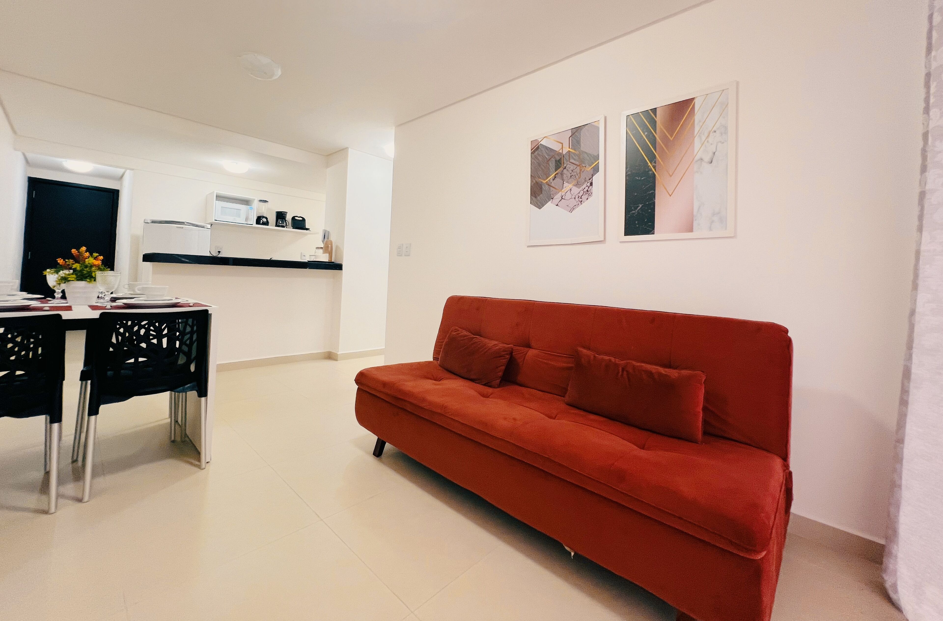 A modern living room with a red sofa, a dining table with chairs, and a kitchen area in the background.