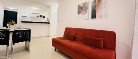 A modern living room with a red sofa, a dining table with chairs, and a kitchen area in the background.