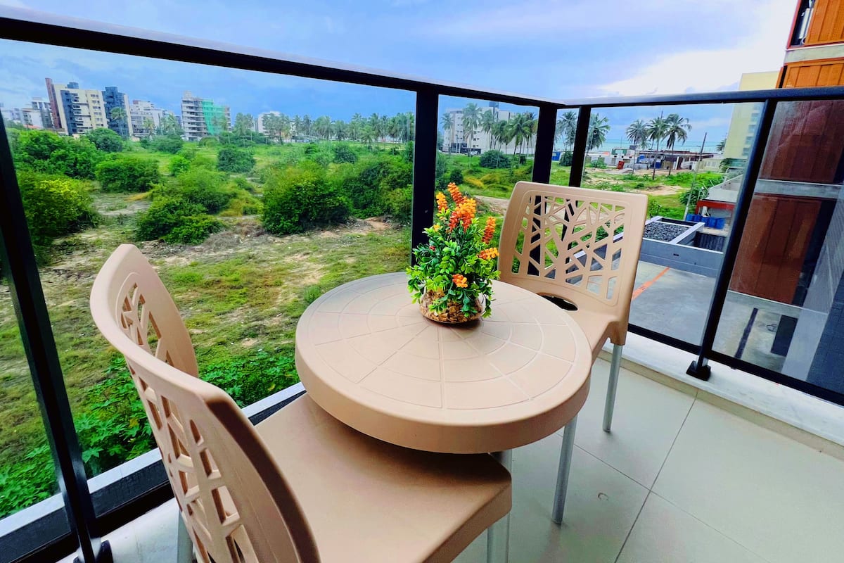 Ein Balkon mit Tisch und Stühlen, einem Blumentopf und Blick auf eine Stadtlandschaft mit Gebäuden und Grünflächen.