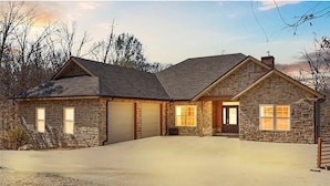 Une maison en pierre avec un garage, une allée et un porche à l’avant.