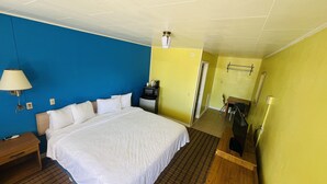 A hotel room with a large bed, a desk, a chair, and a microwave. - Crown Inn (Raton)