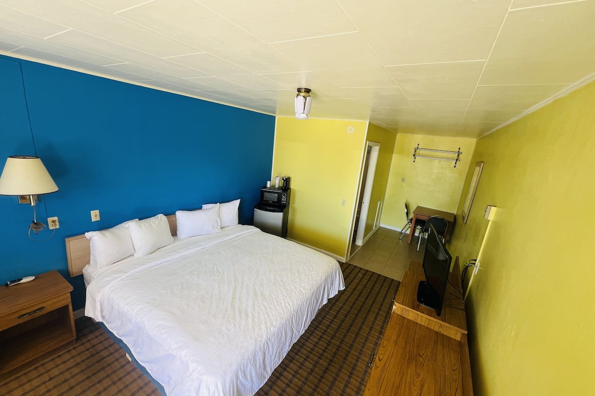 A hotel room with a large bed, a desk, a chair, and a microwave.