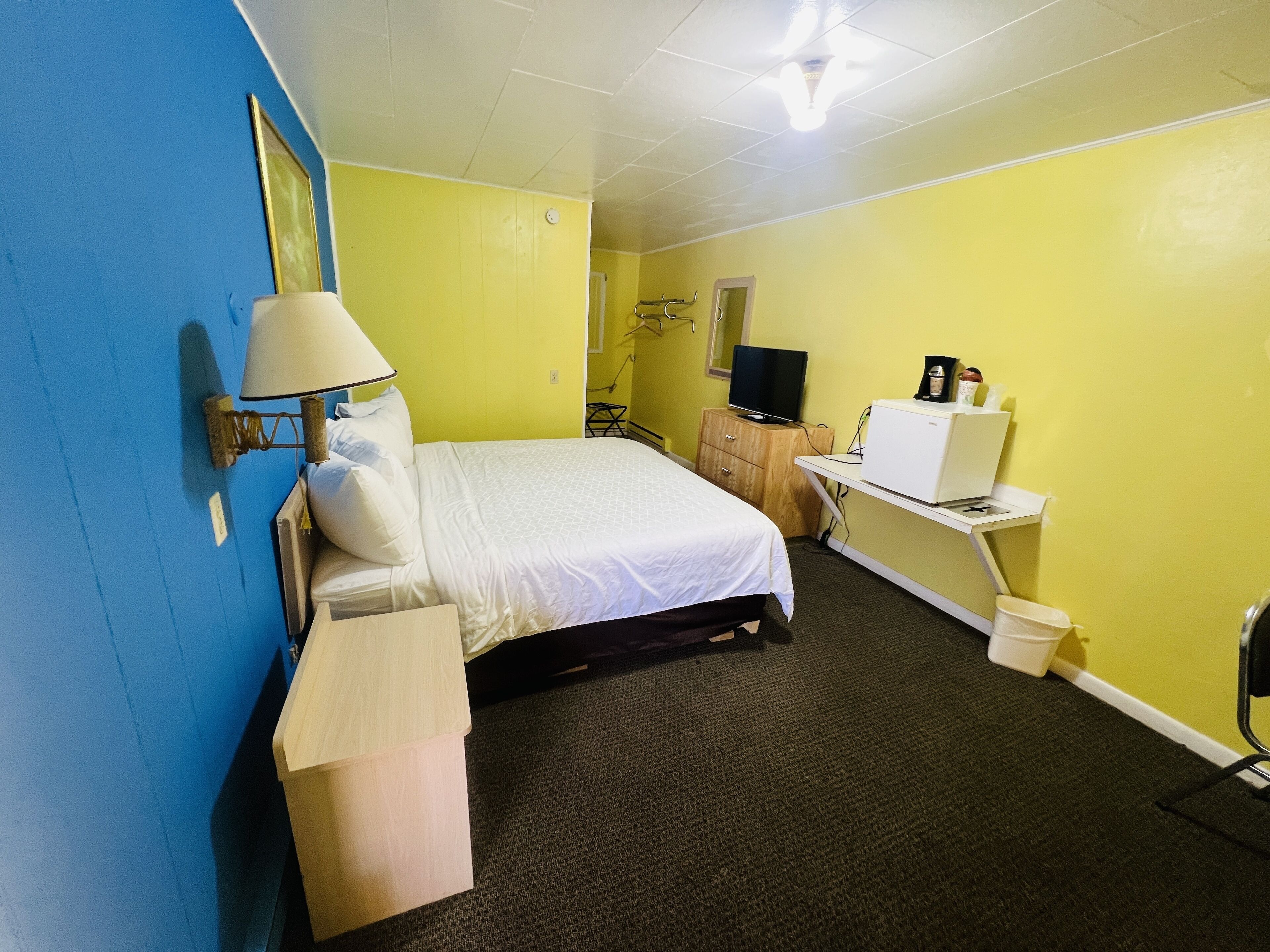 A hotel room with a bed, a desk with a computer, a TV, and a coffee machine.