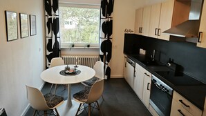 A modern kitchen with a dining table and chairs, a window with black and white curtains, and wooden cabinets. - 3 Zimmer Ferienwohnung 80 qm (Bamberg)