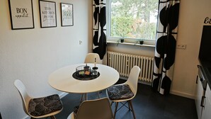 A dining area with a round table and four chairs, each with a patterned cushion. There are three framed signs on the wall, and a window with black and white curtains. - 3 Zimmer Ferienwohnung 80 qm (Bamberg)