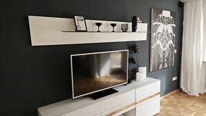 A modern living room with a flat-screen TV, white console, and decorative items on a black wall. - 3 Zimmer Ferienwohnung 80 qm (Bamberg)