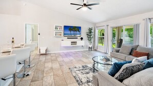 Un salon spacieux comprenant un coin repas, un ventilateur de plafond, un téléviseur à écran plat et une grande fenêtre donnant sur l’extérieur.