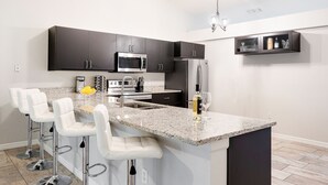 Une cuisine moderne avec des meubles de couleur sombre, un îlot central doté de tabourets, un four à micro-ondes et un réfrigérateur.