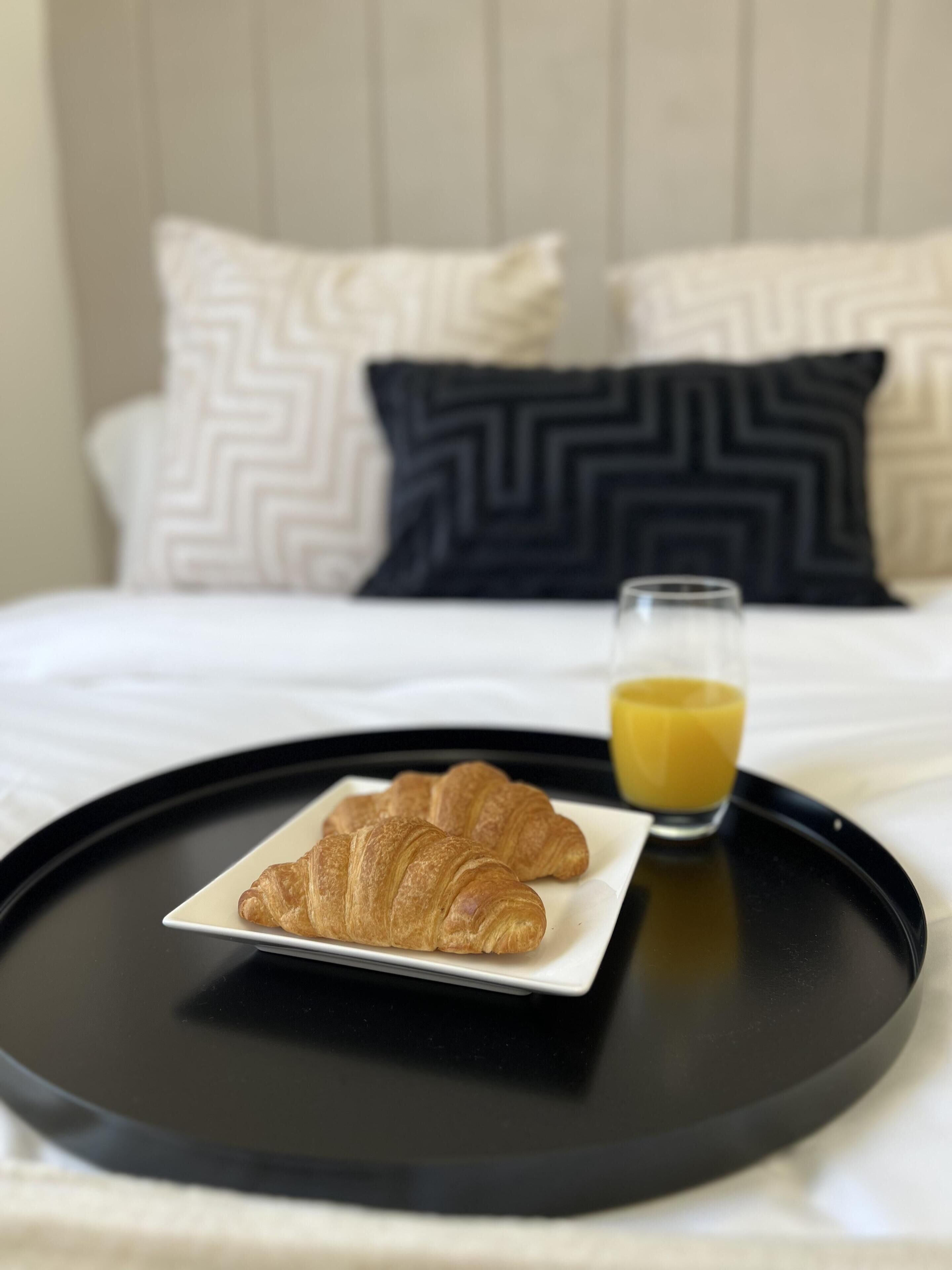Un plateau avec des croissants et un verre de jus d’orange, posé sur un lit agrémenté d’oreillers à motifs.