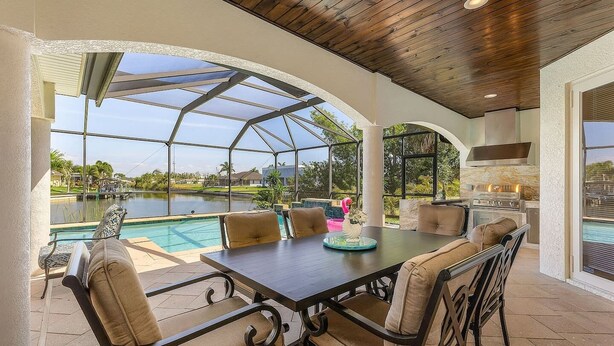 Eine Außenpatio mit Pool, einem Esstisch mit Stühlen und Grillplatz.