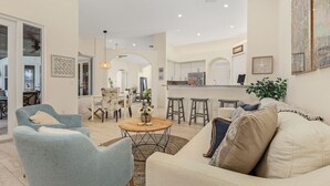 Ein geräumiges Wohnzimmer mit einem hellblauen Sessel, einem beigefarbenen Sofa mit Zierkissen und einem Holztisch.