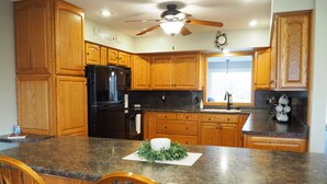 A kitchen with wooden cabinets, a black refrigerator, granite countertops, and a ceiling fan. - Family-friendly Home with large backyard and game room (Coshocton)