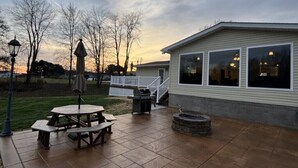 A patio with a picnic table, a fire pit, and a covered seating area. - Family-friendly Home with large backyard and game room (Coshocton)