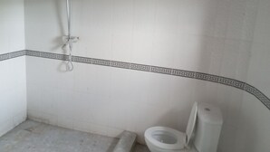 A bathroom with a shower, toilet, and a patterned border on the floor. - Captivating 1-bed Lodge in Accra (Accra)