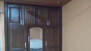 A large wooden wardrobe with multiple doors and drawers, a mirror, and a small shelf. - Captivating 1-bed Lodge in Accra (Accra)