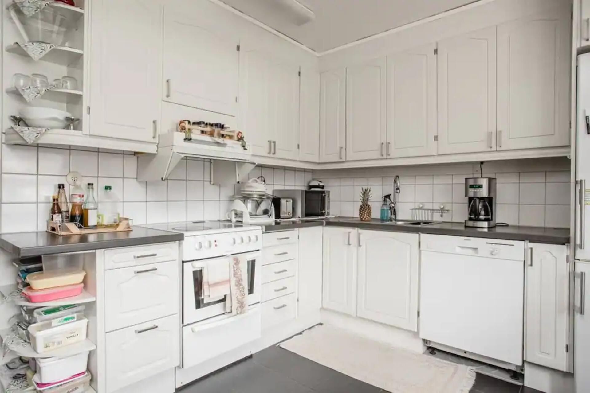 A modern kitchen with white cabinets, a stove, microwave, and a coffee maker.