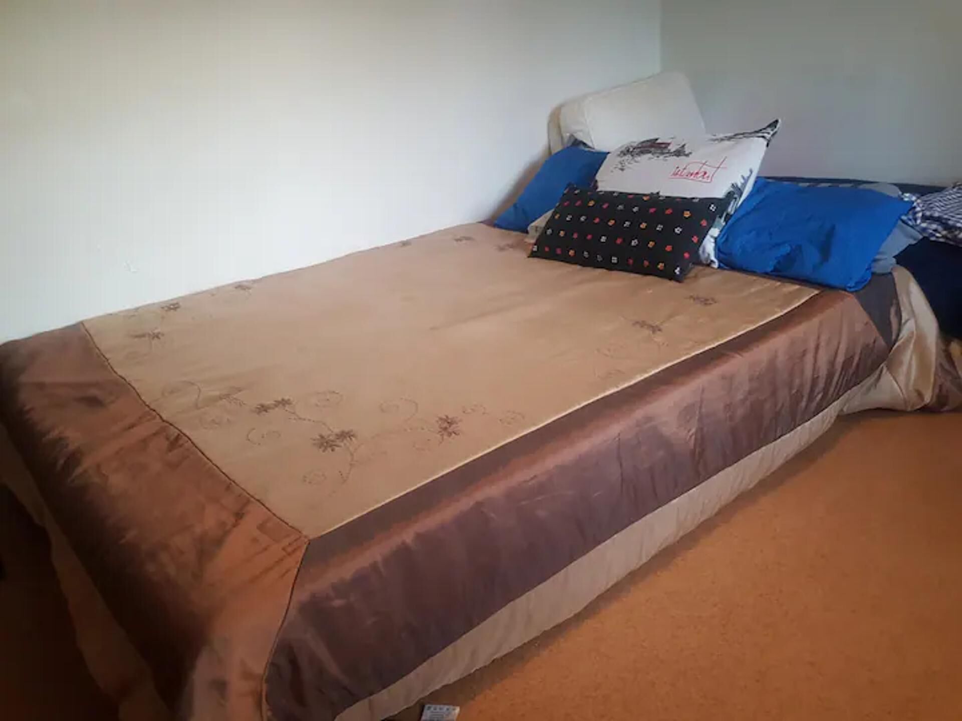 A single bed with a brown and beige bedspread, two pillows, and a blue blanket.